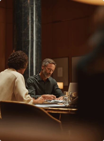 Dois profissionais analisam documentos juntos em uma reunião em ambiente corporativo.