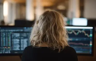 Profissional analisa gráficos financeiros em múltiplos monitores.