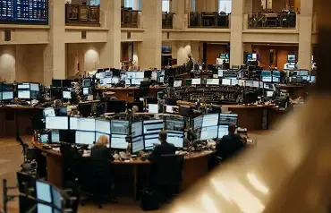 Salão de operações de uma bolsa de valores com estações de trabalho repletas de monitores e operadores em atividade.