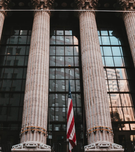 Fachada neoclássica da Bolsa de Valores de Nova York, com colunas imponentes e bandeira americana ao centro.