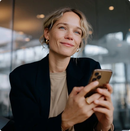 Profissional sorridente segura smartphone em ambiente corporativo, com olhar voltado para cima.